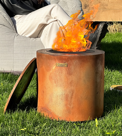 Corten Steel Eco Fuego Fire Pit Lit in a garden with person relaxing 