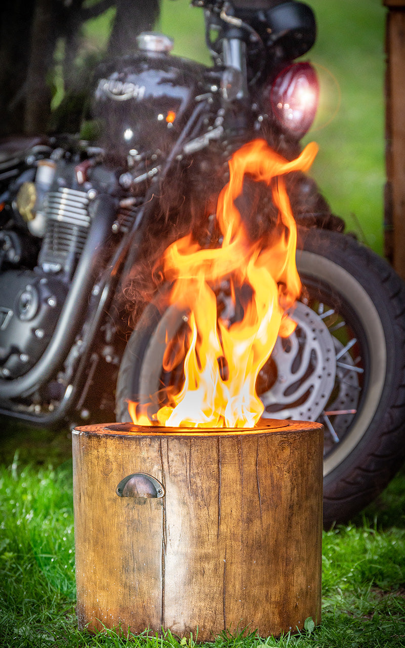 El Fuego fire pit in garden, with motorbike behind. Fire Pit has large flame from vegetable candle, being the most eco-friendly fire pit in UK.