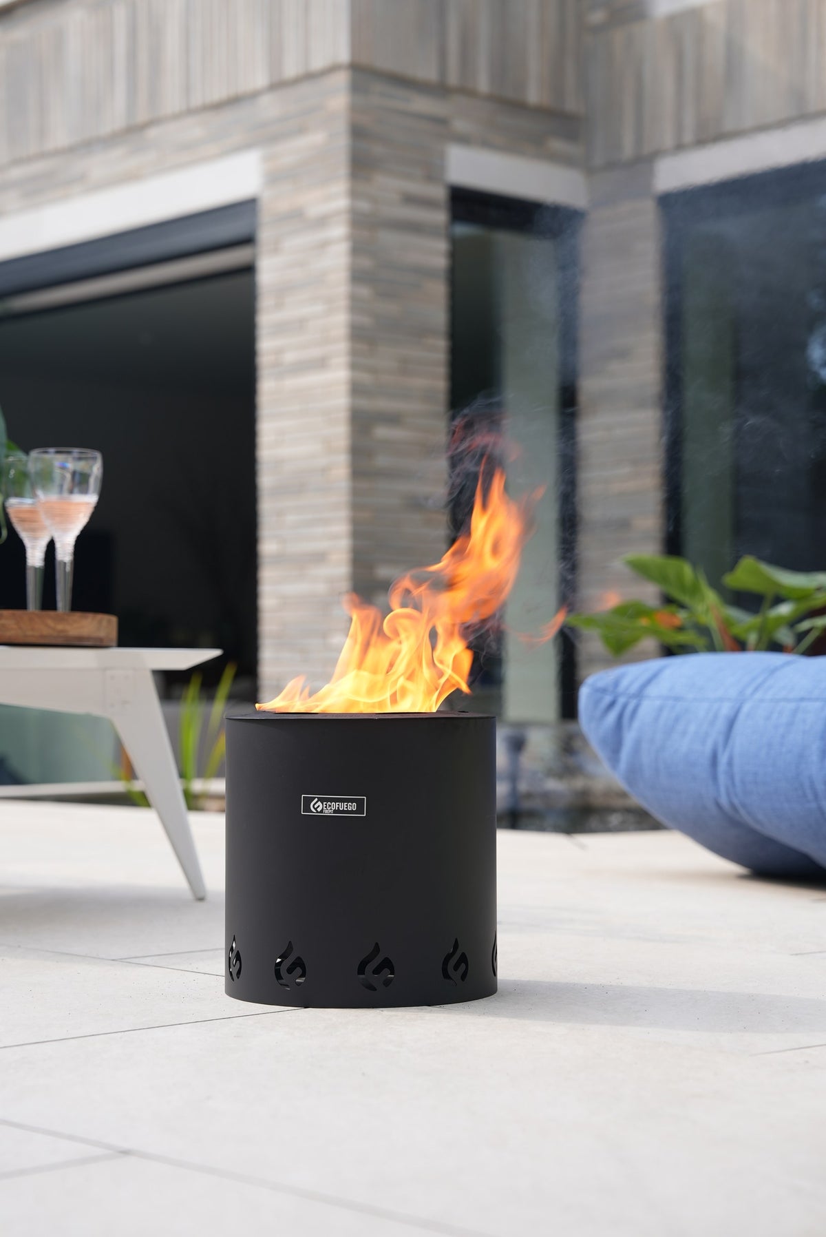 An ECOFUEGO El Campo burning on a patio beside someone sitting with their feet up